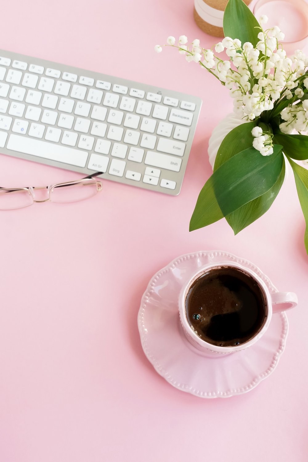 Pink flat lay top view women's office desk . Female workspace with laptop, white spring flowers lilies, accessories, glasses, cup of coffee on pink background. Copy space